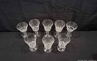 Eight clear glass stemmed goblets arranged on black background