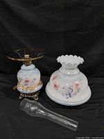 Lamp components laid out: shade, base, burner ring, chimney