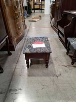 Overall view of one footrest showing wood frame, upholstered top, size relative to surroundings