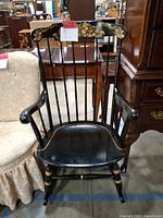 Front view of black rocking chair showing floral motif, spindles and overall style