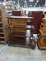 Frontal view showing four wooden shelves and metal scrollwork sides