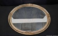 Front view of oval mirror showing ornate gold-tone frame and glass