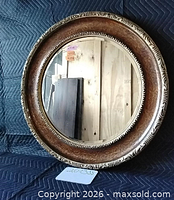 Front view of round mirror showing ornate brown and gold frame and glass