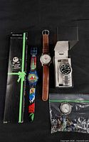 Group shot showing all five items: boxed Nightmare Before Christmas watch, plastic cartoon watch, brown-strap chronograph-style watch, boxed diver-style watch, bead bag with watch head