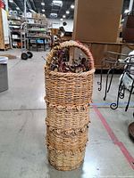 Full view of tall woven wicker basket standing upright with foliage inside