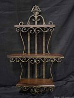 Full frontal view showing three wooden shelves within ornate scrolled metal frame and crest