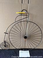 Front view of metal penny-farthing wall decor against cardboard backdrop