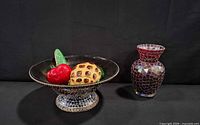 Bowl filled with three faux fruits beside mosaic vase