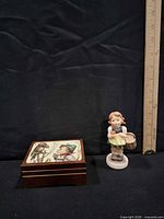 Music box closed and figurine beside ruler for scale