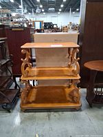Front view of three-tier wooden shelf with scroll supports