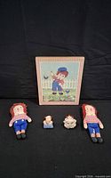 Lot overview showing all items: two cloth dolls, framed picture, two small figurines