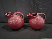 Two red Hall China ball pitchers side by side