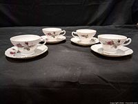 Four teacups and four saucers displayed on black backdrop