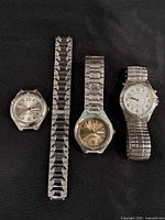 Overview of three wristwatches and separate metal bracelet on black background