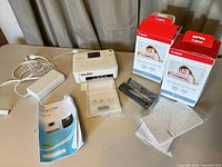 Overall lot showing printer, power adapter, paper tray, manual, USB cable and two boxed ink/paper sets