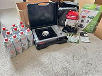 Stove, lantern, fuel canisters, mantles, manuals, box, bags arranged on floor