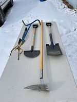 Four long-handled garden tools laid out on table