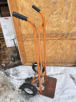 Full view of orange hand truck standing upright on snow-covered ground