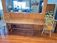 Drop-leaf dining table with one leaf extended, two matching spindle-back chairs shown
