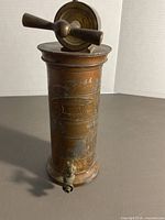 Front view of entire brass irrigator showing cylindrical body, spigot, and crank