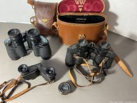 Overall lot showing Zeiss, Wray, Tasco binoculars, leather cases and loose lens