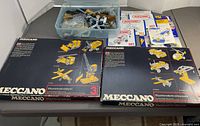 Overall view of lot showing two Meccano boxes, tub of parts and manuals