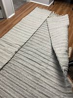 Full view of folded 8' x 10' gray handwoven rug showing rib texture and fringe