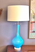 Full view of light blue glass table lamp with white shade on wood surface