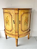 Front view of wooden demilune cabinet showing floral panels and handles