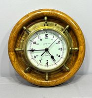 Full view of brass ship’s wheel clock in oak frame