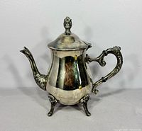 Full view left side of teapot showing feet, spout, lid and finial