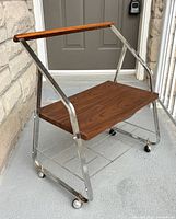 Front angled view showing chrome frame, laminate shelf, wooden handle, casters