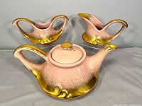 Front view teapot with creamer and sugar bowl displaying pink luster and gold trim