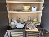 Cabinet view showing boxed Chantal fondue set, ceramic mixing bowl, glass pieces and plates