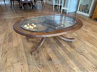 angled view of entire oval coffee table showing wood frame, glass inset and wrought iron scroll base