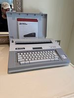 Front angled view of typewriter with lid open showing keyboard and documentation