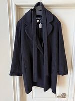 Front view of black Sunny Choi coat hanging, tie draped, shows overall style and texture