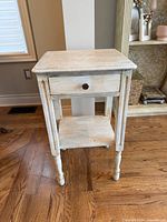 Full view of whitewashed wood side table showing drawer, lower shelf and turned legs