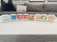All eight Fire King milk glass mugs lined up showing front designs