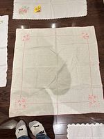 square linen cloth with pink embroidery and nearby smaller embroidered doily