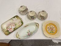 All nine porcelain pieces laid out: three teacups on saucers, two trays, one decorative plate