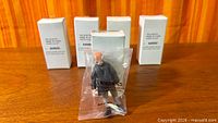 Five white mailer boxes and one bagged figure displayed