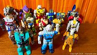 Group shot of all 13 Transformers Action Masters figures standing on wooden surface