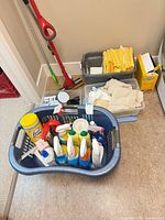 Overview of basket with spray cleaners, wipes, Swiffer box, and two totes of cloths