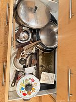 Drawer showing entire assortment of stainless pans, lids, enamel pot and booklet
