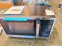 Front view of Insignia stainless/black microwave on counter with manual on top