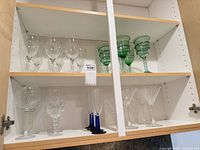 Cabinet shelf with clear wine glasses, green swirl goblets, blue-stem flutes, cut-crystal glasses