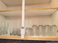 Shelf showing four pilsner glasses, four upright highball glasses, eight upside-down tumbler glasses