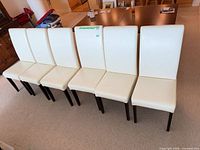 Front view of six matching cream faux leather dining chairs in a row