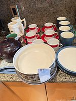 Group of plates, cups, mugs, teapot, coffee pot and serving bowl on countertop